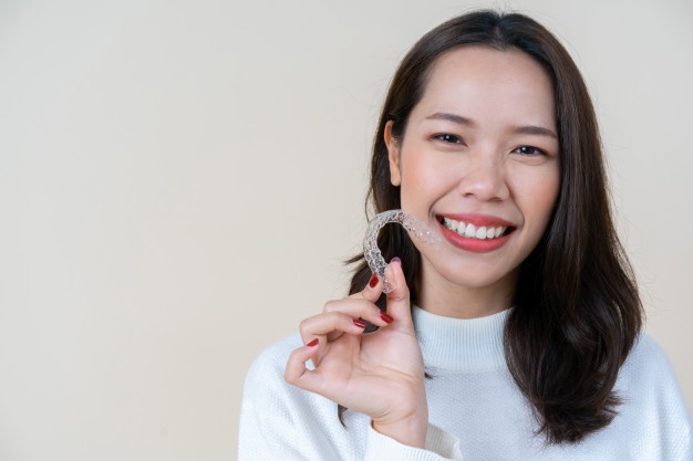 asian-woman-smiling-with-hand-holding-dental-aligner-retainer_42708-608